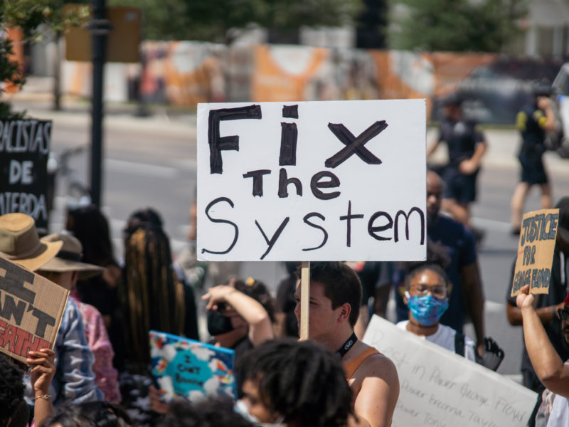 protester hodling sign saying fix the system